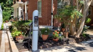 EV charger in corner of parking lot near garden. 