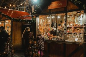 Outdoor rustic holiday market stall with salesman and two shoppers. 