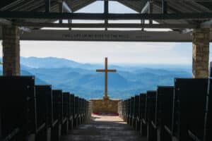 Open air chapel with wooden cross overlooking mountain view.