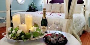 Chocolate dipped strawberries near flameless candles and a bottle of champagne in front of a four poster bed. 