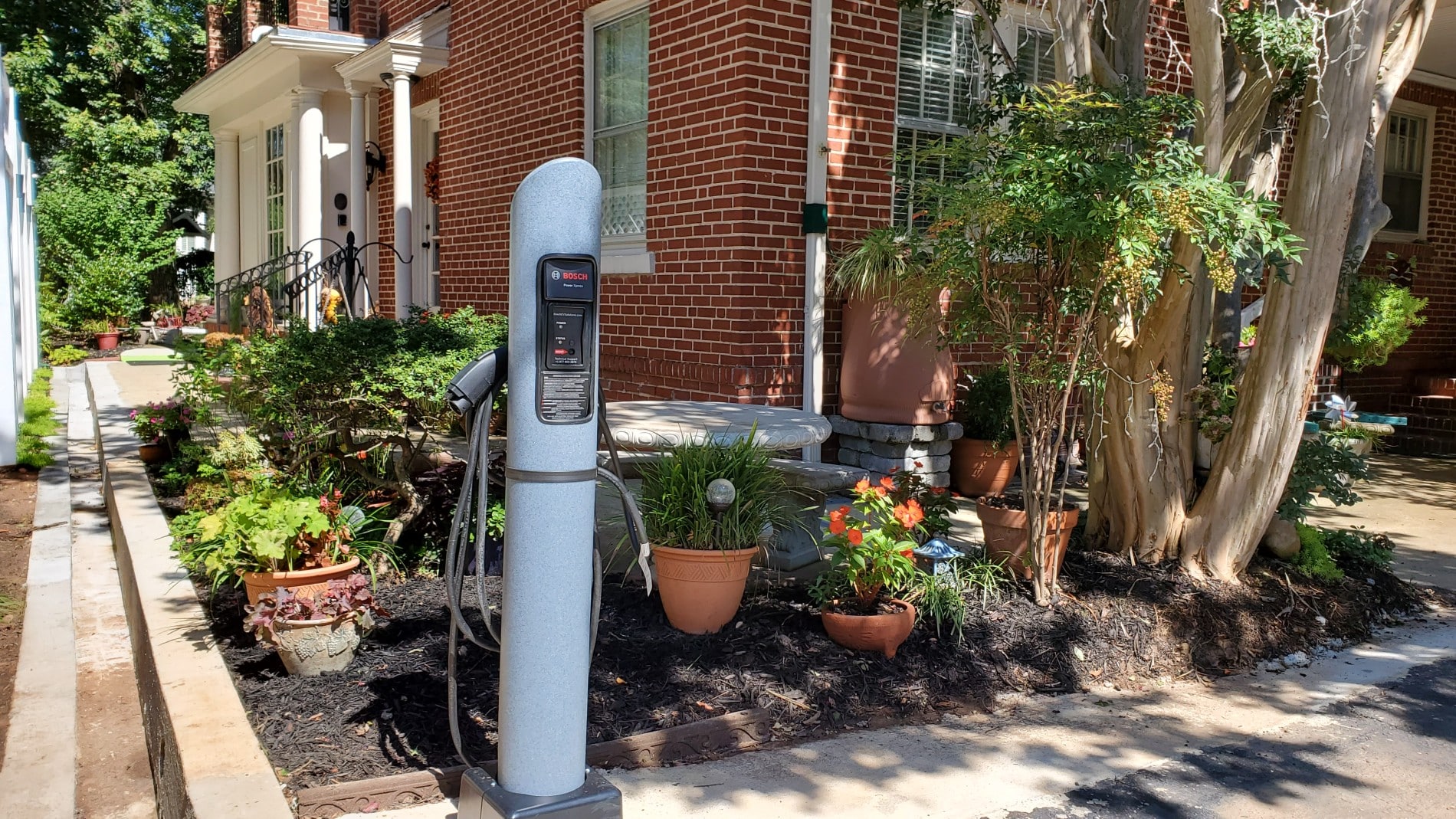 EV charger in corner of parking lot near garden.