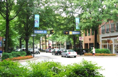 Greenville's Main street with cars, shopping, stop light, and man crossing the street.