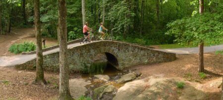 A man and woman on bikes riding over a stone bride in wooded area.