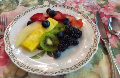 Fresh fruit plate with berries, pineapple, melon, and kiwi on fine china plate on top of set table