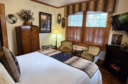 King size bed with antiques, two chairs and fireplace.