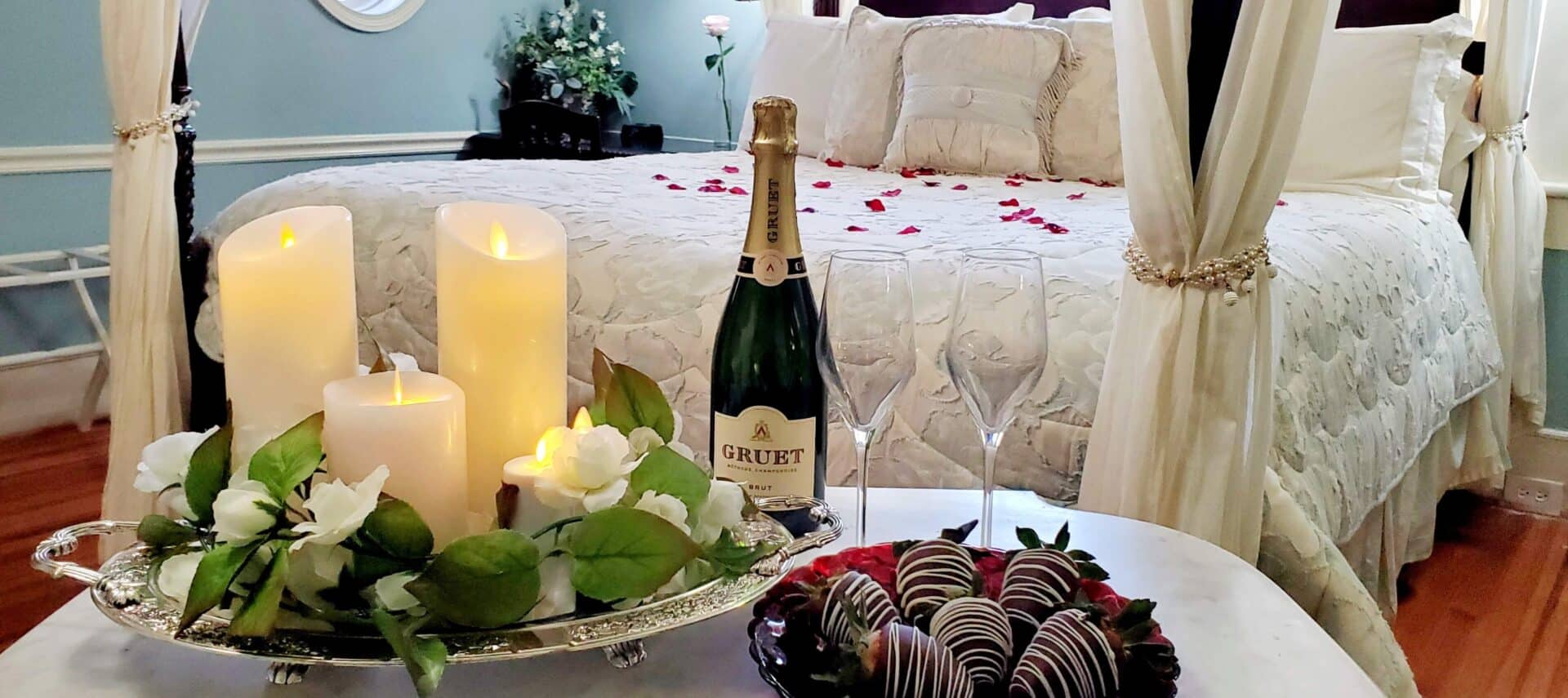 Chocolate dipped strawberries wit champange in front of four-poster bed with flameless candles