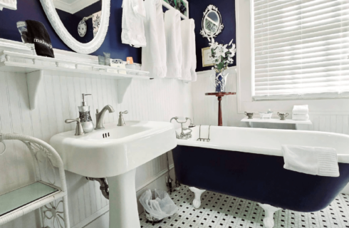 Bathroom with clawfoot tub in dark blue by sink and window.