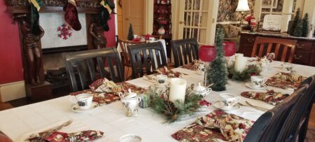 Table set for eight with Christmas linen near fireplace hung with stockings